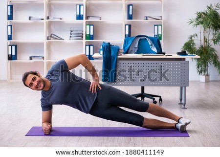 Young handsome employee doing sport exercises in the office