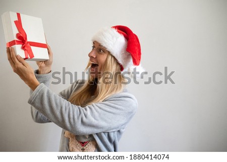 Woman on white background wearing Christmas pyjama and cap holding box gift with red tape. Happy to get and give the gift. Feel fairy tale and magic. new year emotional and mood.