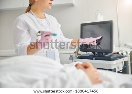 Cropped photo of a female cosmetologist in latex gloves tipping the touch screen of a beauty machine