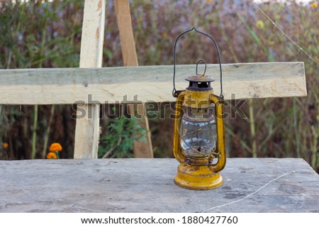Old yellow oil lantern is on wooden bench. It's an equipment for camping or being a light in a dark.