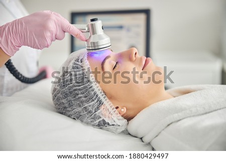 Calm young lady in a gauze cap lying with her eyes closed during the purple light therapy Royalty-Free Stock Photo #1880429497