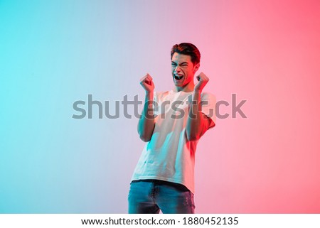 Crazy happy, mad. Young caucasian man's portrait on gradient blue-pink studio background in neon light. Concept of youth, human emotions, facial expression, sales, ad. Half length, copyspace.