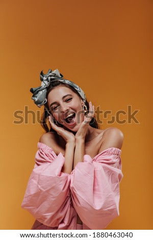 Fashionable cute woman with green stylish bandana and earrings in pink modern blouse looking into camera and rejoices on isolated background..