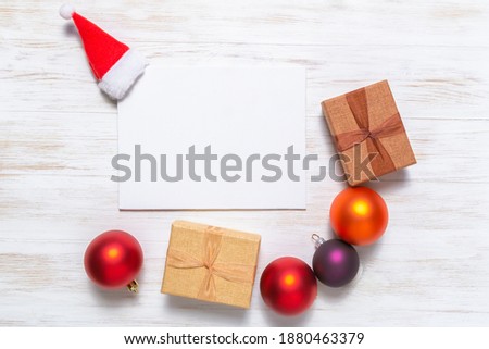 Blank greeting card with Santa Claus hat, balls, and gift boxes. Holiday mockup. Christmas concept. Flat lay, top view, copy space