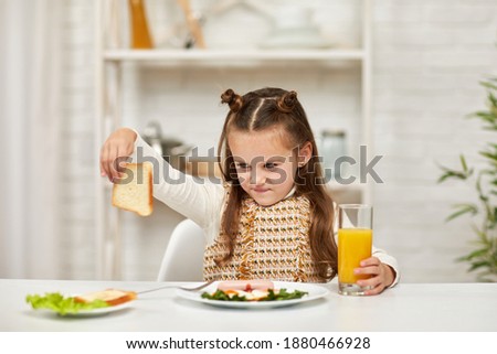the child does not want to have breakfast. little girl looks at the sandwich with disgust