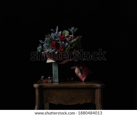 A closeup picture of a bouquet made of roses, hollies and thistles on a wooden table with Christmas decoration in front of black background.