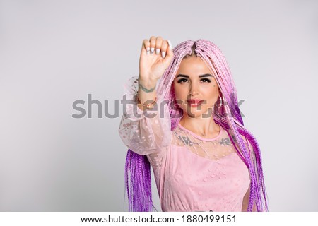 Portrait of a young serious modern girl with pink braids showing a fist up on a white background