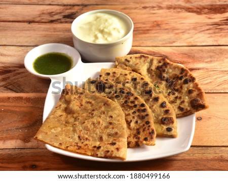 Aloo Paratha or Indian Potato stuffed Flatbread. Served with fresh curd and mint chutney. isolated over a rustic wooden background, selective focus