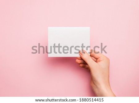 Hand with white blank card on pink background. Copy space, space for text. Mockup template for design.