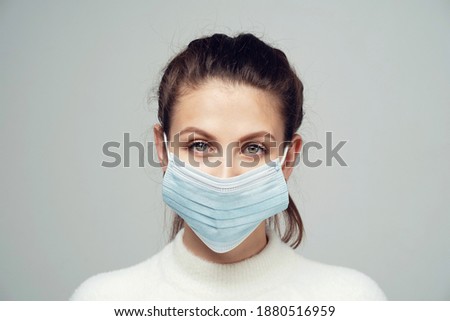 face mask protection against coronavirus, pandemic, virus, epidemic, bacterium, covid 19, covid 21. a young brunette woman in a white jacket looks at the camera and smiles. space to copy.
