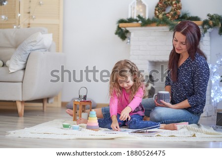 Positive cute young woman mom sits on floor in a festive studio and plays with little girl.. Good Christmas mood concept