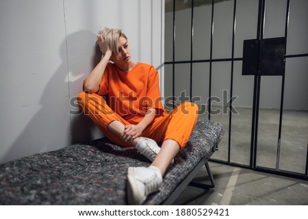 Girl convicted drug dealer in an orange jumpsuit in his cell on a prison bunk. Royalty-Free Stock Photo #1880529421