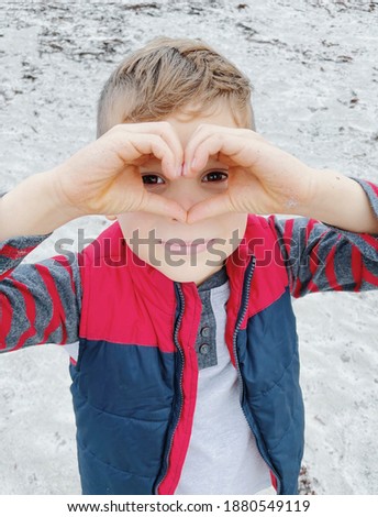 Adorable boy making shape of heart with hands for Valentine's Day. Cute child holding hands in heart shape framing on nature background. Token of love.