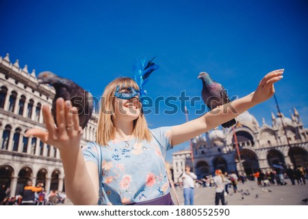 Portrait smiling young woman in Venice, Italy in Venetian mask feeds pigeons on St Mark Square. Concept travel.