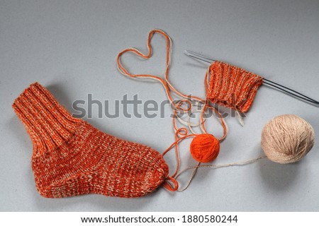 Knitted sock with yarn and knitting needles, heart made of thread, top view, gray background-the concept of warm cozy things for winter days