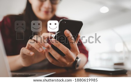 Customer service evaluation concept. smiling Asian female Is using a smartphone And she is pressing face emoticon smiling in satisfaction on virtual touch screen. Royalty-Free Stock Photo #1880619985