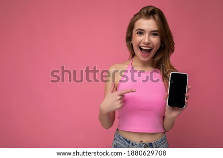 Photo of beautiful smiling young woman good looking wearing casual stylish outfit standing isolated on background with copy space holding smartphone showing phone in hand with empty screen display for