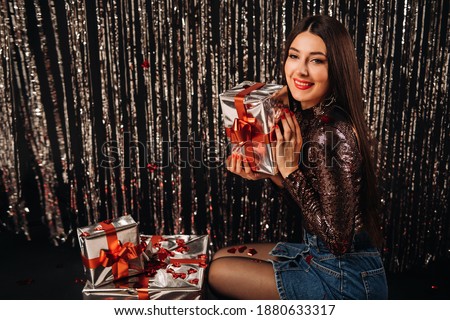 a girl in a shiny jacket and skirt with gifts on a silver background in the form of rain