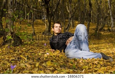 Young handsome man laying in autumn forest