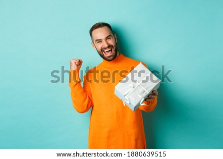 Holidays and celebration concept. Excited man receiving gift, looking happy at present and smiling, standing over blue background Royalty-Free Stock Photo #1880639515