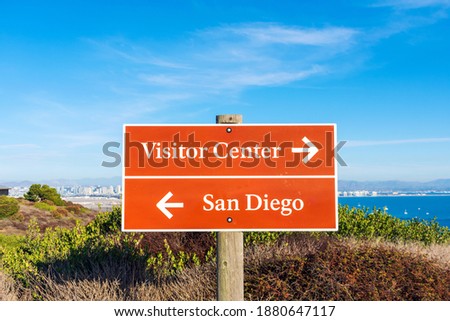 San Diego and Visitor Center brown guide road sign with white lettering and directional arrows. Background San Diego Bay and citiscape