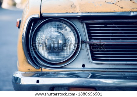Close up and front view shot with copy space of chrome grill and front light of yellow retro car in grunge condition with rust and dirt shows beautiful detail and old day american style design.
