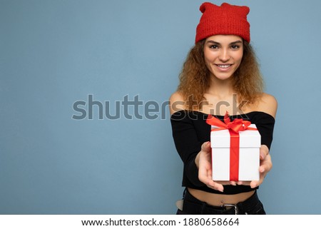 Beautiful happy young brunette woman isolated over colourful background wall wearing stylish casual clothes holding gift box and looking at camera