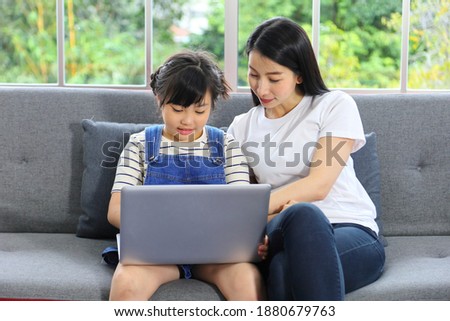 Asian mother teaching her daughter to learn from online class using laptop for homeschooling and education concept