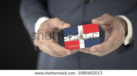 Businessman holding plastic bank card with printed flag of the Dominican Republic, fictional numbers