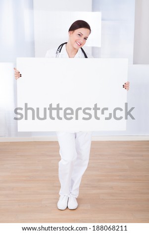 Portrait of happy young female doctor presenting blank billboard in hospital