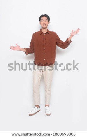 Full body handsome attractive young man inbrown shirt with white pants , white sneaker, showing both hands open palms

