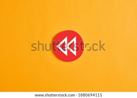 Red round circle with a rewind button against yellow background.
