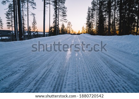 Beautiful natural environment white northern destination with road for traveling, scenic picture of winter season forest with frost and snow. Sunset in the wood between the trees in winter period.