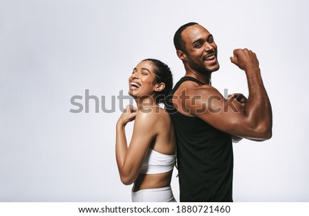 Smiling fitness couple standing back to back against white background. Fit couple showing arm muscles standing together. Royalty-Free Stock Photo #1880721460