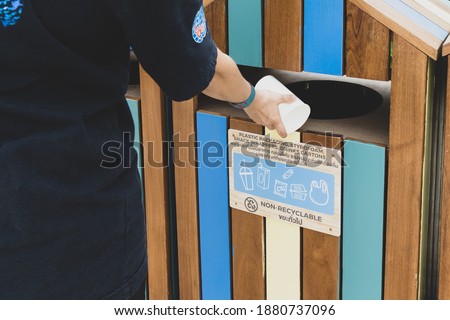 Woman throwing plastic or paper cup into the wooden dustbin with sign non recyclable. Concept of separation rubbish before drop to garbage bin to save the world, environment care.