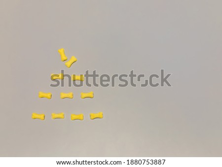 Yellow bones in the form of a Christmas tree on a gray background. Sweets, dragees, food. Dog food, copy space, top view