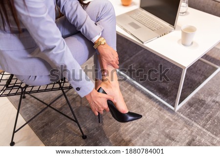 Tired businesswoman woman sitting on chair and taking shoes off after hard day at work. Businesswoman taking off high heels shoes after work at home.