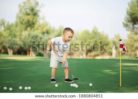 little Boy playing golf and hitting ball by putter on green grass. Royalty-Free Stock Photo #1880804851
