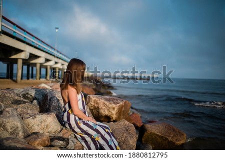 portrait of a girl who sits on stones at the pier near the sea