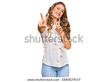 Young blonde girl wearing casual clothes smiling looking to the camera showing fingers doing victory sign. number two. 