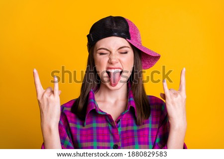 Close up photo of positive funky brown hair teen girl show rock sign tongue out wear pink shirt headwear isolated on yellow color background