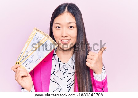 Young beautiful blonde woman holding airline boarding pass smiling happy and positive, thumb up doing excellent and approval sign 