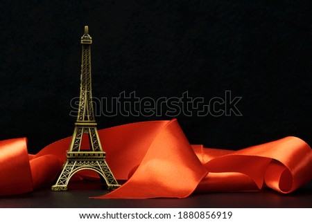 A statuette of the Eiffel Tower surrounded by a red ribbon on a black background. The concept of romance, love, travel.