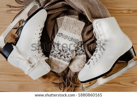 Winter flatlay with white skates for figure skating, a warm scarf and mittens