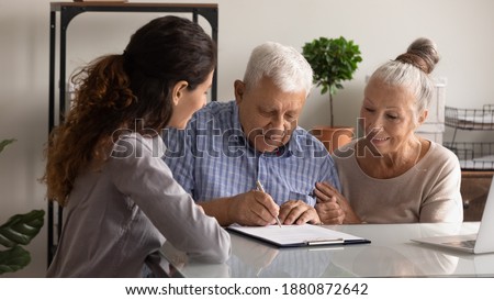 Happy senior man and woman clients sign deal buy house take bank loan mortgage together. Excited elderly couple spouses put signature on document close health insurance agreement in office.