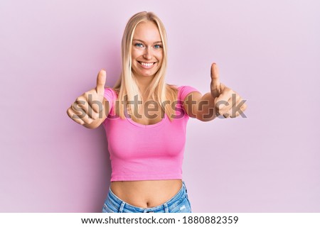 Young blonde girl wearing casual clothes approving doing positive gesture with hand, thumbs up smiling and happy for success. winner gesture. 