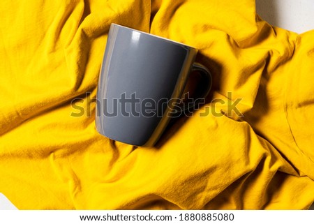 Ultimate gray mug on bed with illuminating yellow fabric coverlet with wrinkles and hard light