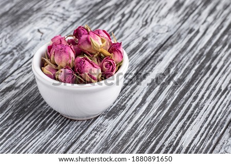 Dried damask rose buds in small bowl on black wooden table.