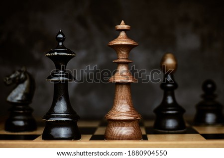 Black queen and king chess pieces facing each other. Checkmate on wooden chessboard. Duel and rivalry concept.