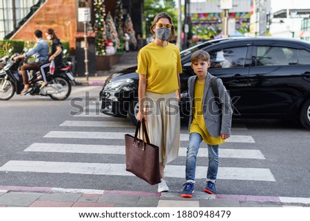 Woman and boy wearing in two colors of 2021 year illumination yellow shirt and ultimate gray protective mask walking on street of city pedestrian crossing. New rules. Travel concept. Protect yourself